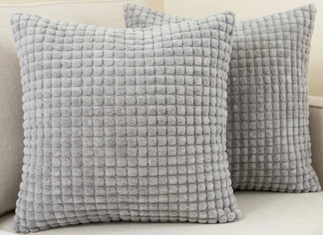 Light grey textured soft velvet jaguard throw pillows with square ribbed pattern, two pieces on beige sofa.