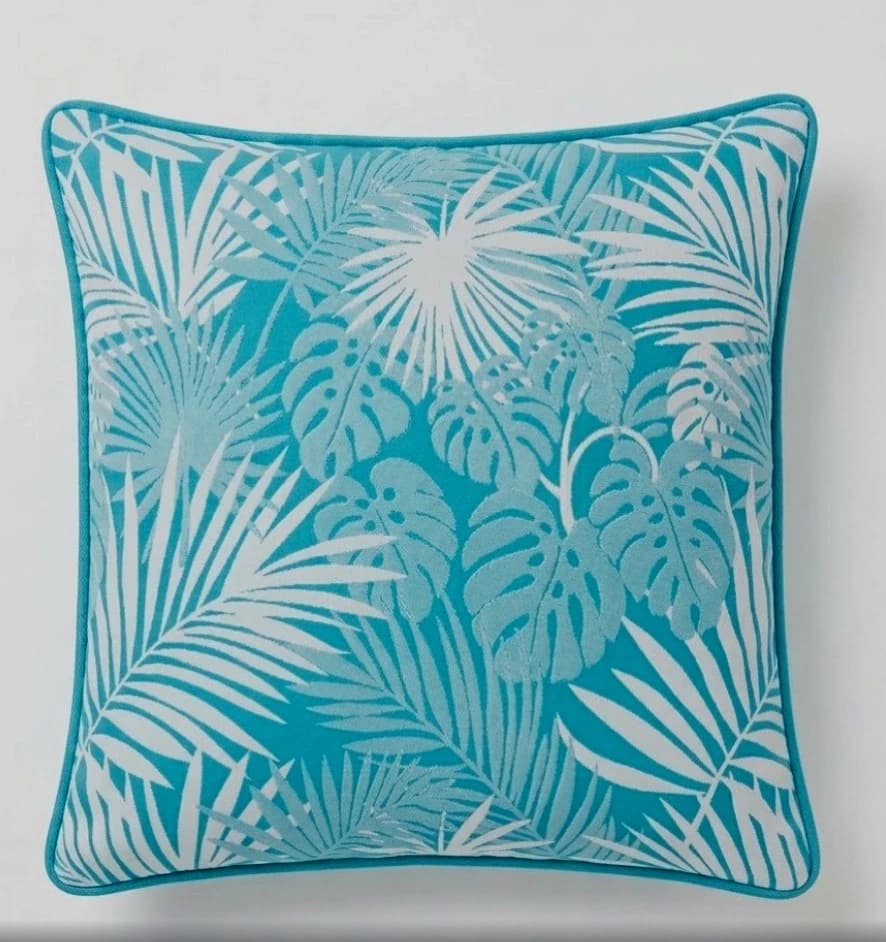 Square teal outdoor pillow covers with white tropical leaf print and blue star border on a light background.