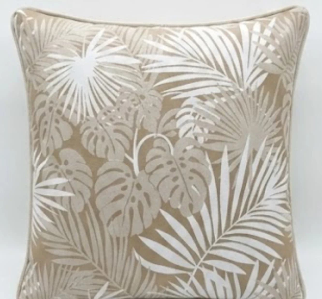 Beige square throw pillow with white tropical leaf print, black stems, and glossy finish on fabric.